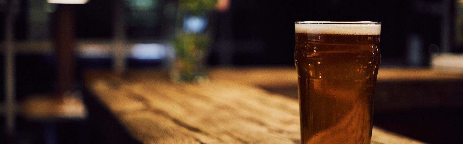 A glass full of beer on the wooden counter of a bar