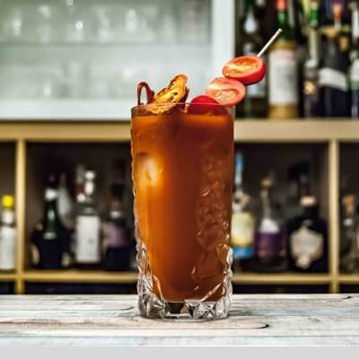 Exotic brown-coloured drink with baby tomatoes in a transparent glass sitting on the counter of the bar