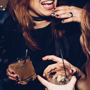 Two women holding a drink each, having fun and chatting